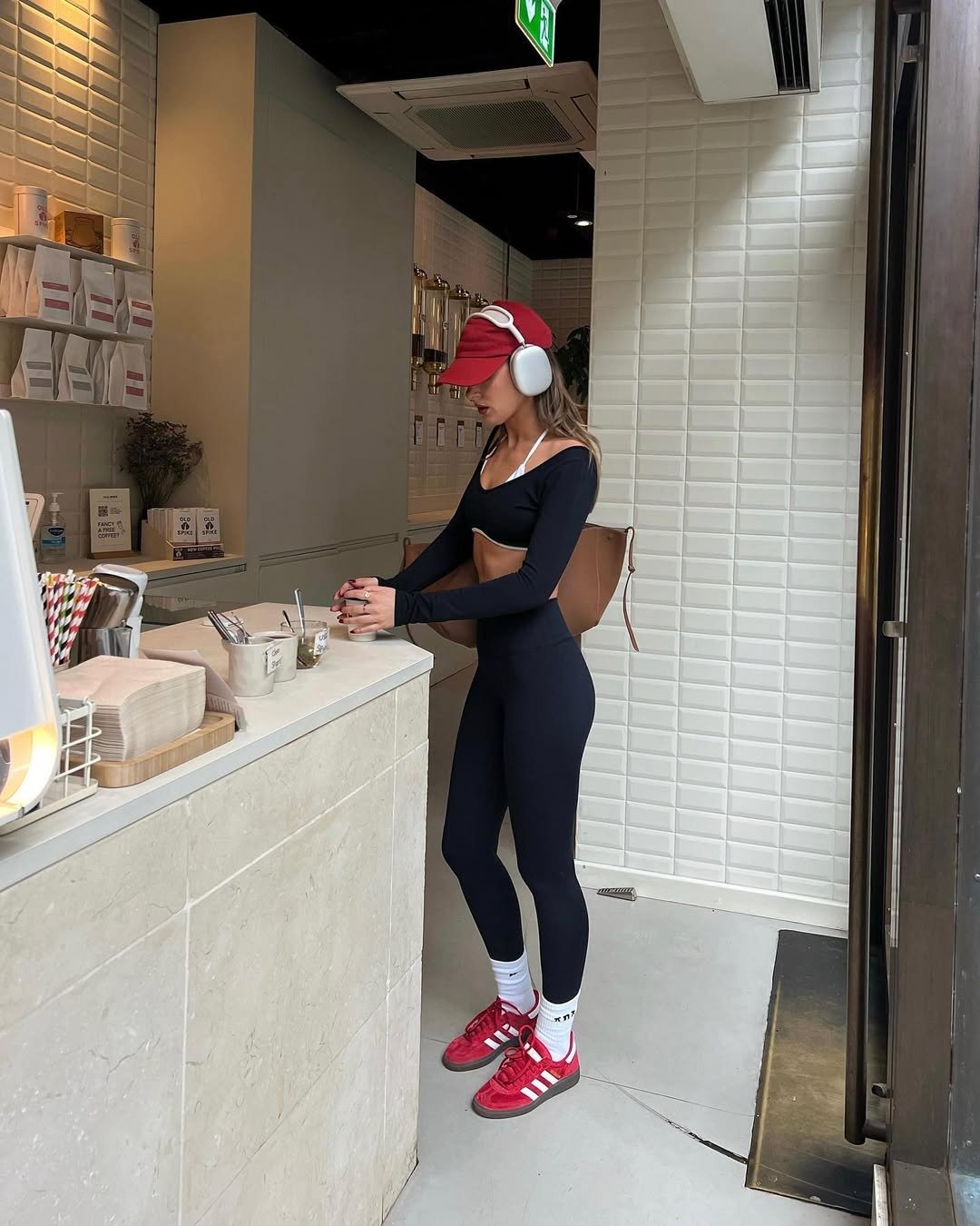 Look para academia feminino com conjunto preto de legging e cropped manga longa em tecido justo, tênis vermelho, boné e