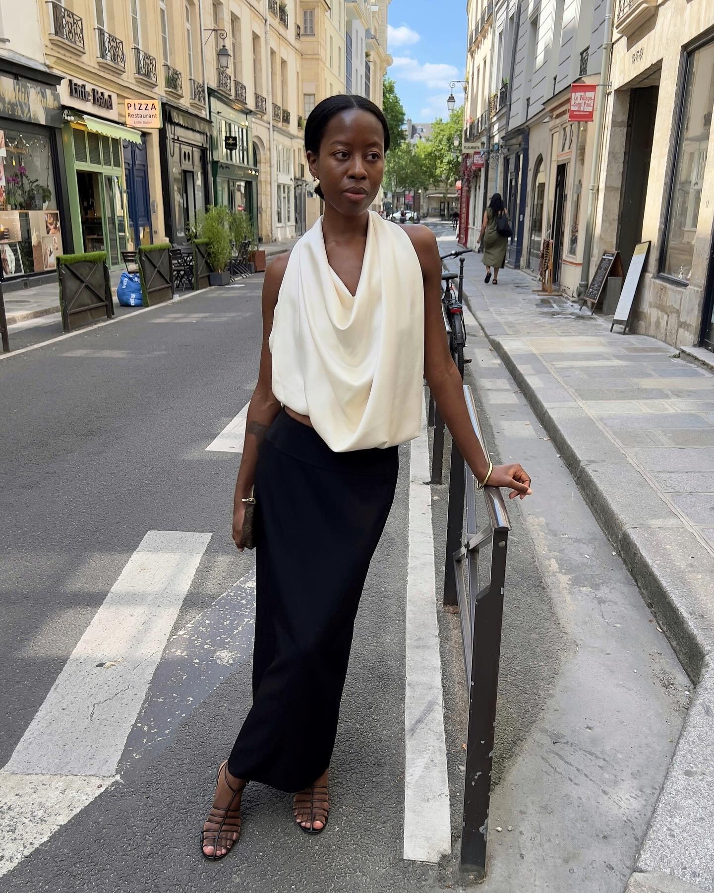 Modelo posa com looks sofisticados usando blusa off-white de tecido fluido com decote drapeado e saia preta longa de corte