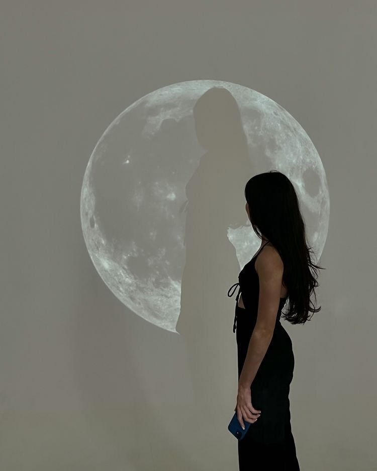 Modelo veste vestido preto justo com recortes laterais e alças finas, posa de perfil contemplando a lua nova de janeiro