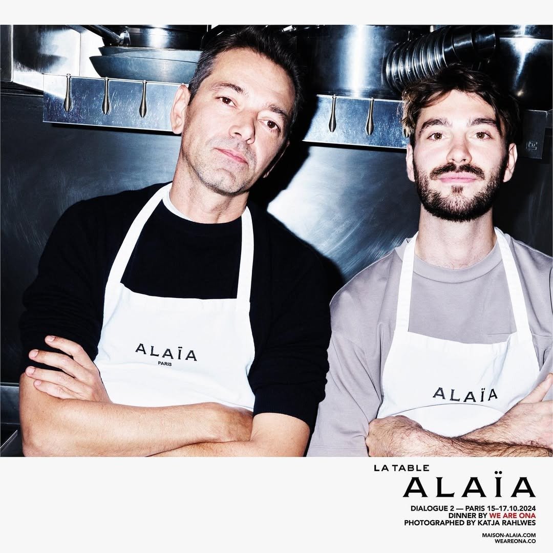 Dois homens posam com aventais brancos Alaïa sobre malhas pretas e cinza, em ambiente metálico que sugere inovação na