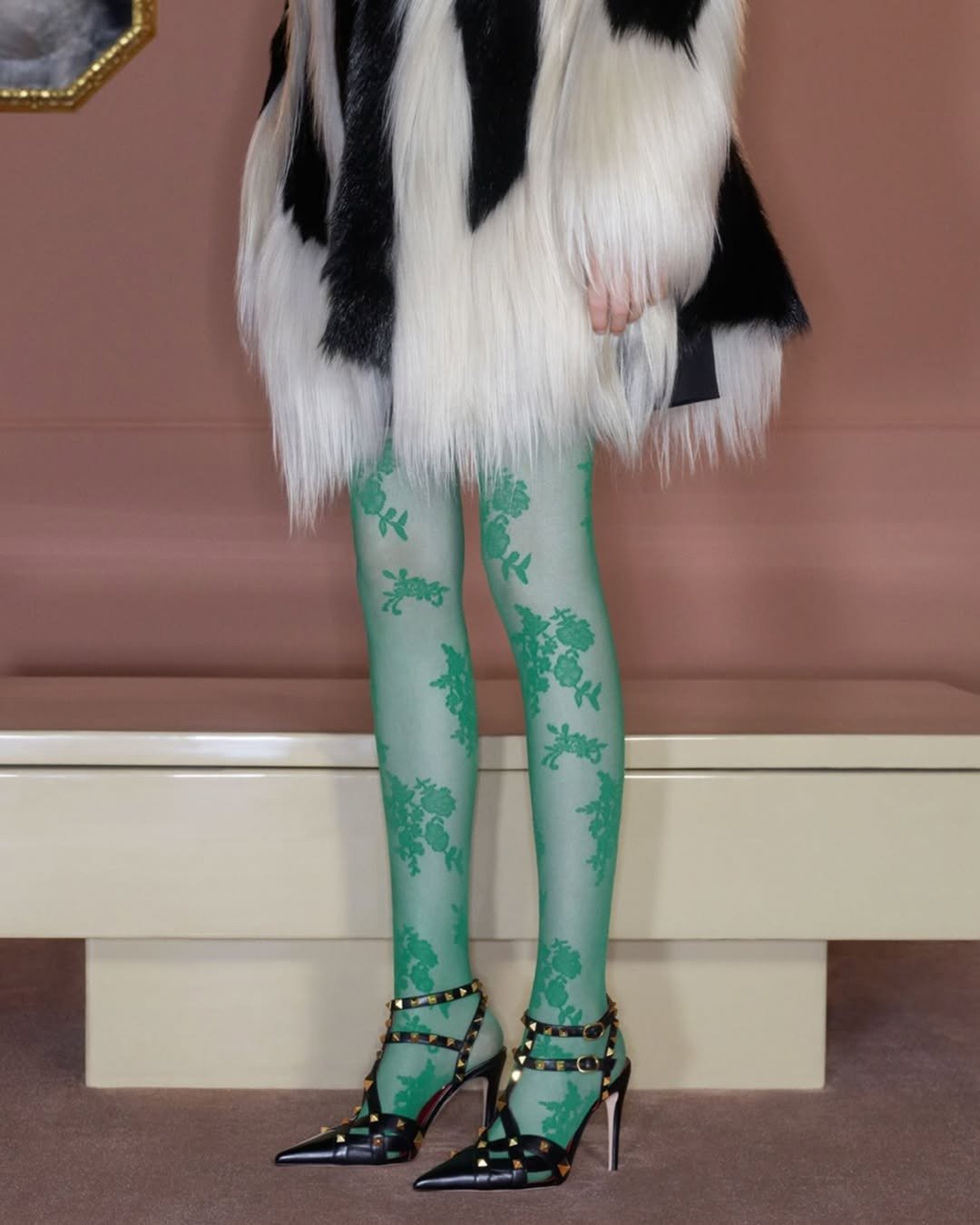 Valentino apresenta look com casaco peludo preto e branco, meia-calça verde floral e scarpin preto com tachas douradas, em