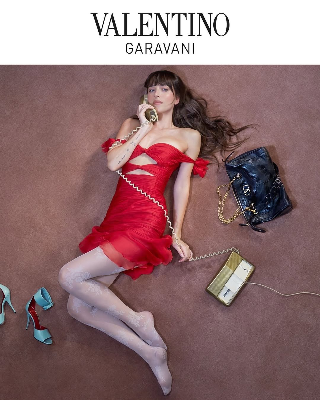 Modelo deitada em vestido vermelho justo com recortes e tecido franzido, meia-calça branca rendada, sapatos azul claro ao