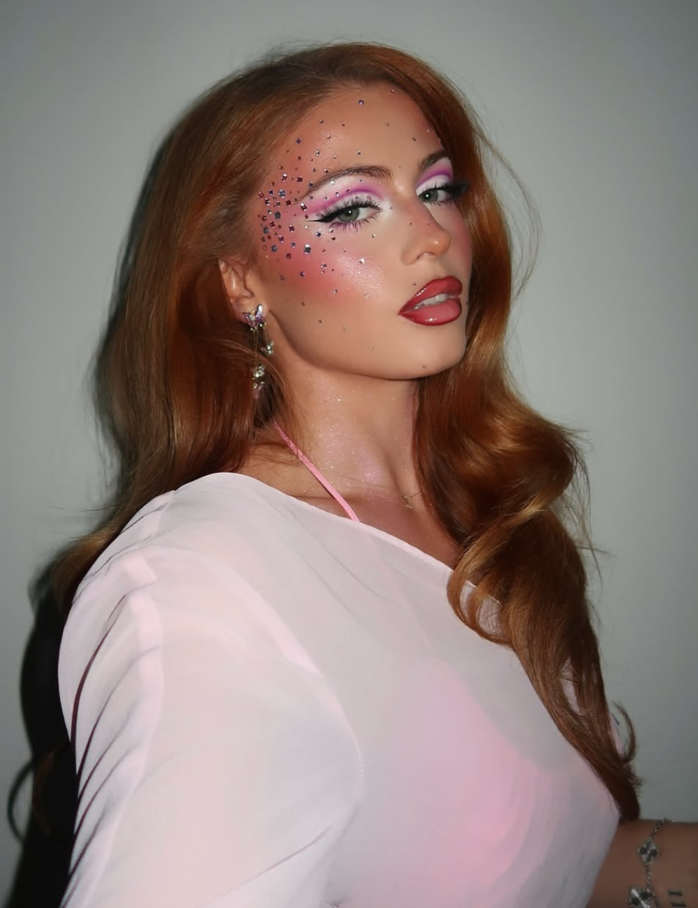 Modelo posa com maquiagens de Carnaval que combinam glitter prateado, sombra rosa vibrante, delineado preto e batom vermelho.