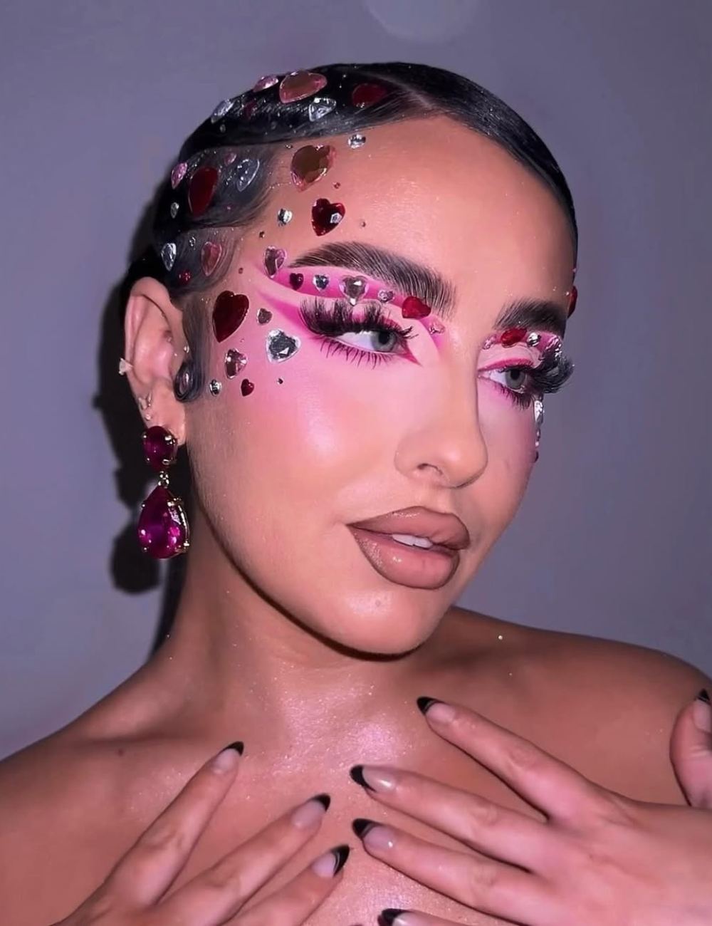 Maquiagens de Carnaval com cristais vermelhos e prateados em formato de coração, sombras pink vibrantes e cílios volumosos.