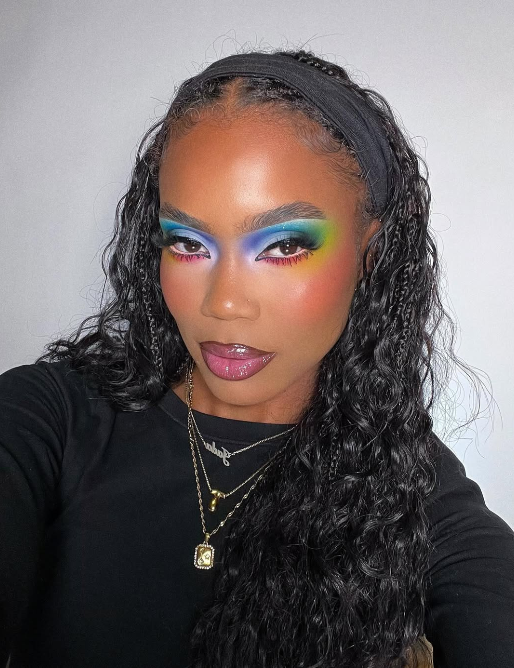 Modelo posa com maquiagens de Carnaval vibrantes em azul, verde e rosa, combinando sombra esfumada, blush rosado e gloss.