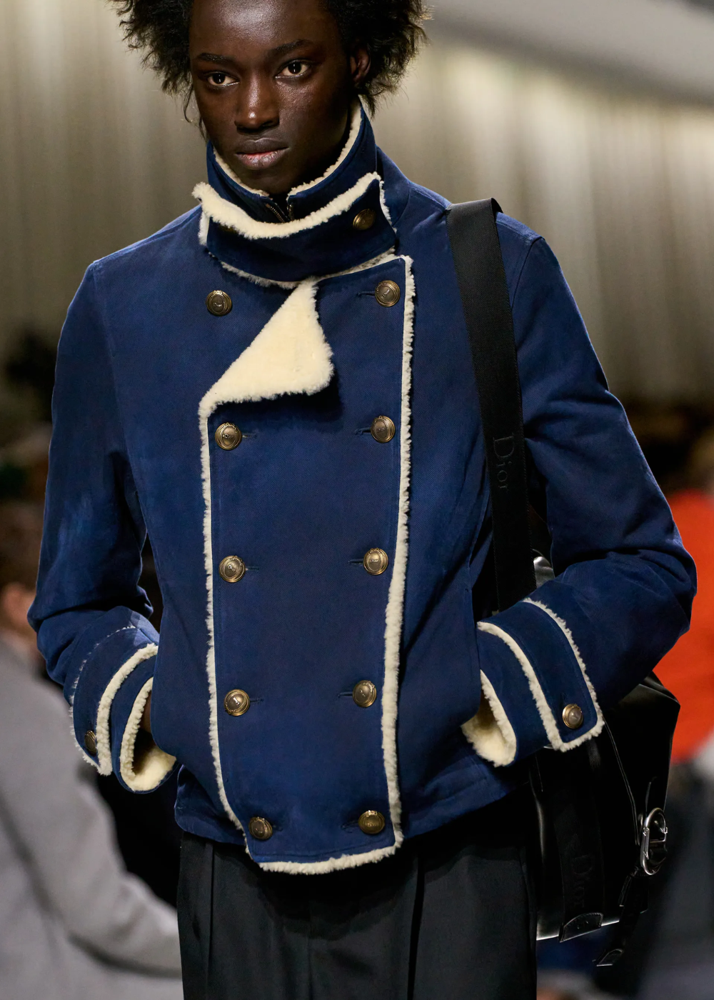 Modelo anda na passarela com jaqueta azul-escuro com botões dourados.