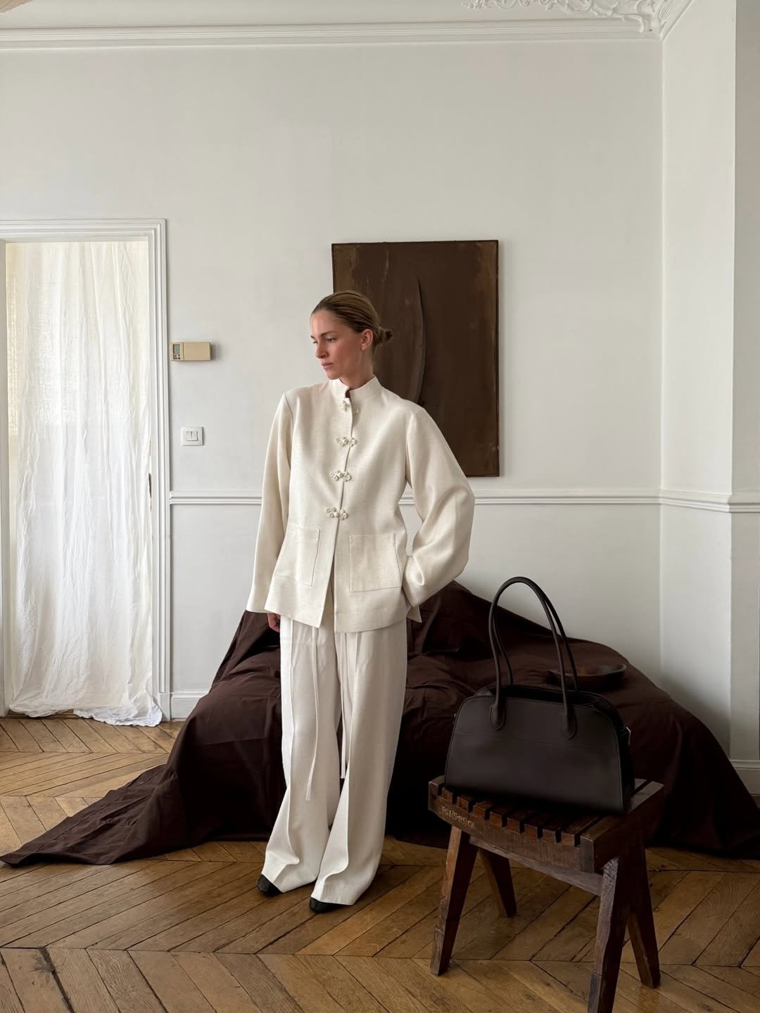 Modelo posa com postura serena em conjunto off-white de tecido fluido, destacando nó chinês nos botões da jaqueta de