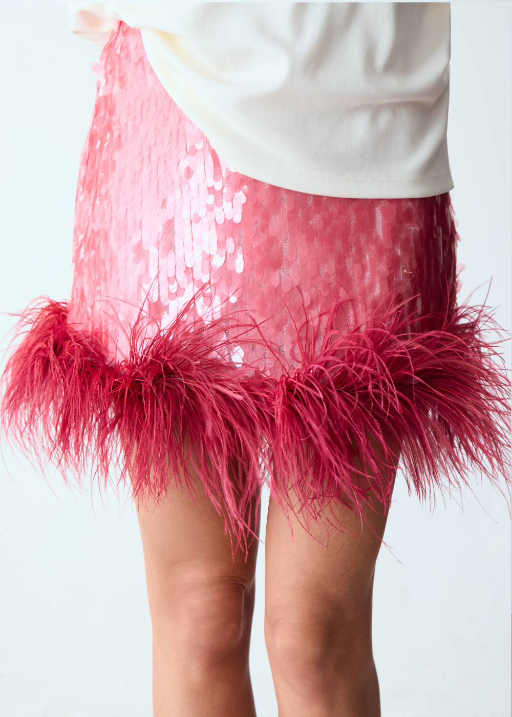 Saia rosa com paetês e barra de plumas vibrantes combina com camiseta branca, criando drop de carnaval cheios de leveza e