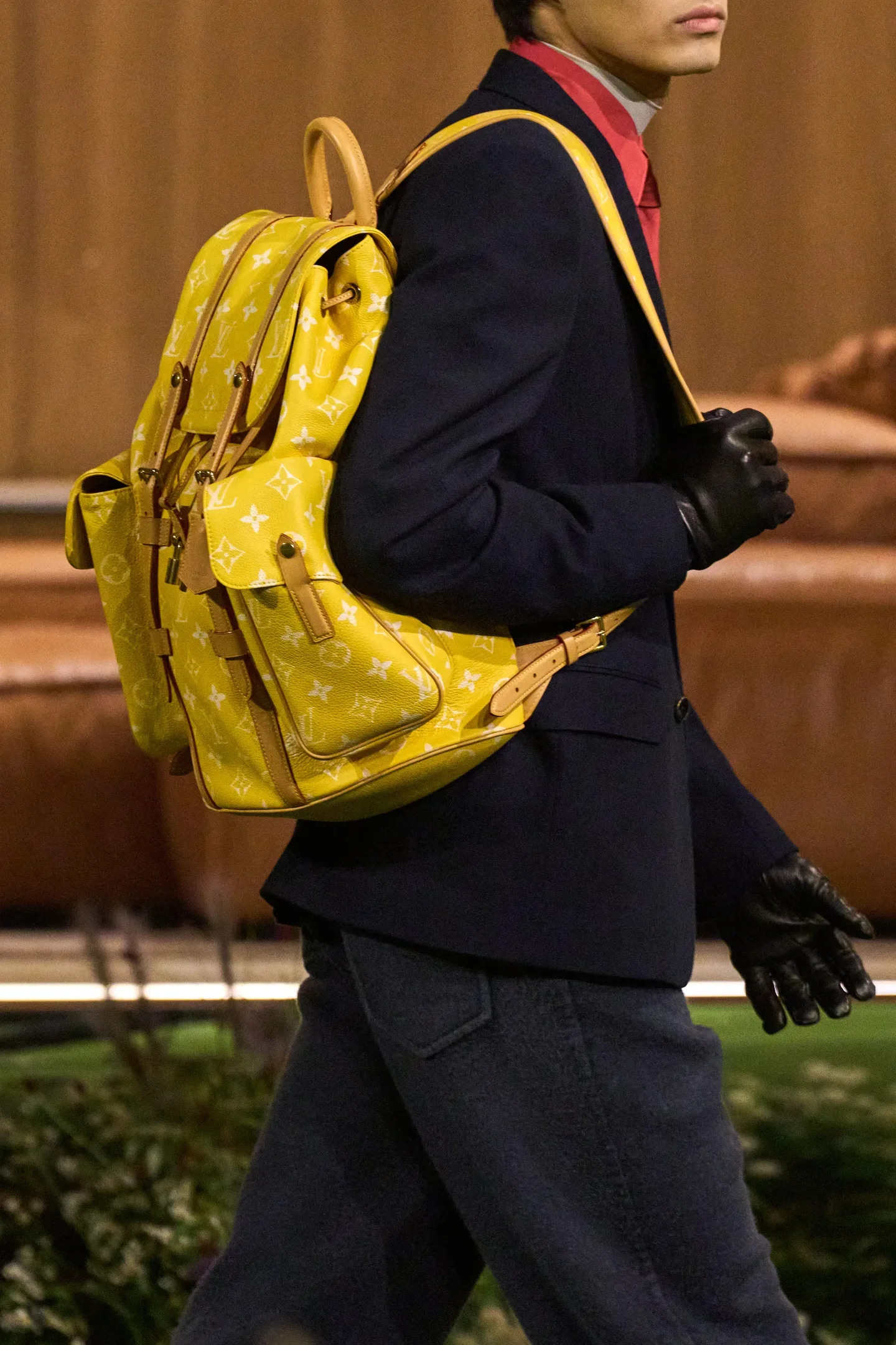 Modelo caminha com postura confiante usando mochila estilosa amarela em couro texturizado com bolsos frontais e detalhes em