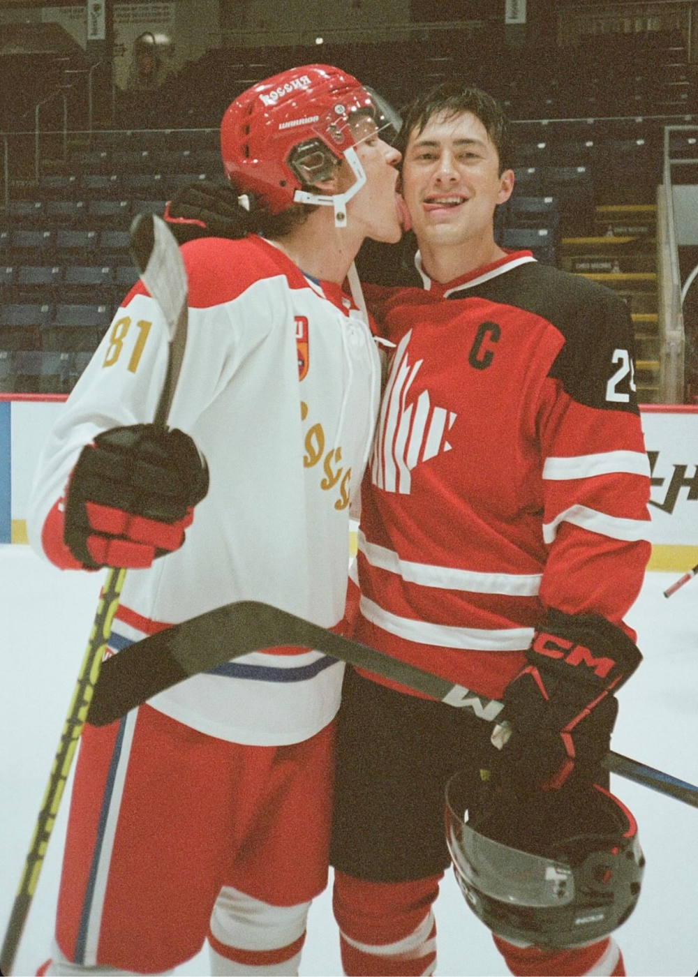 Jogadores de hóquei em gelo vestem uniformes técnicos vermelhos e brancos, com capacete e luvas.