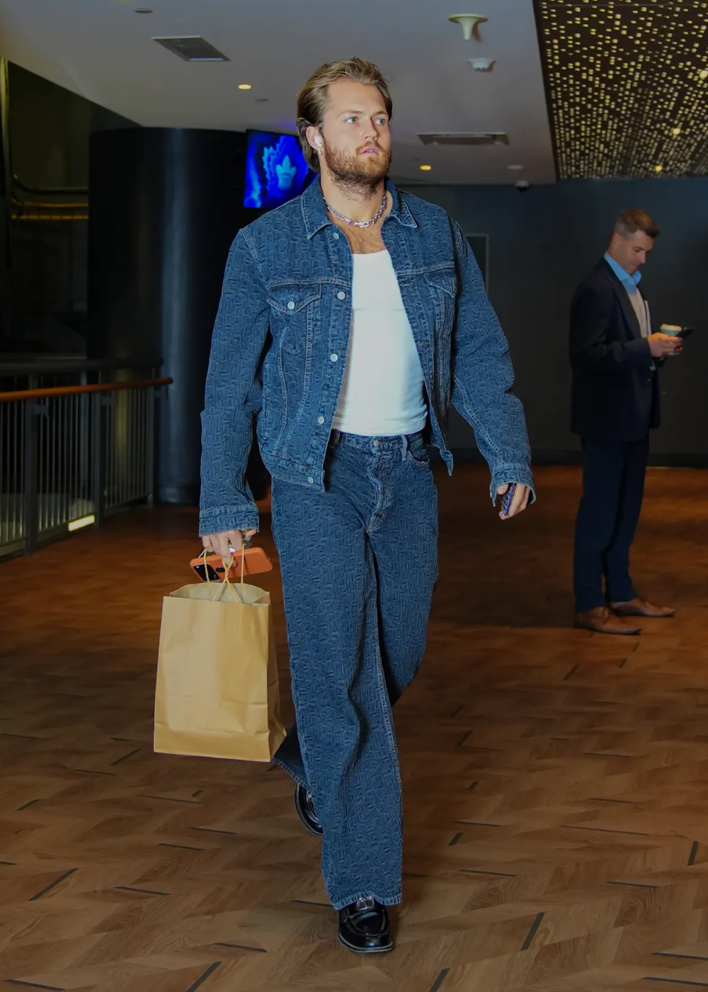 Homem caminha com jaqueta e calça jeans texturizados azul escuro, camiseta branca justa e sapatos pretos.
