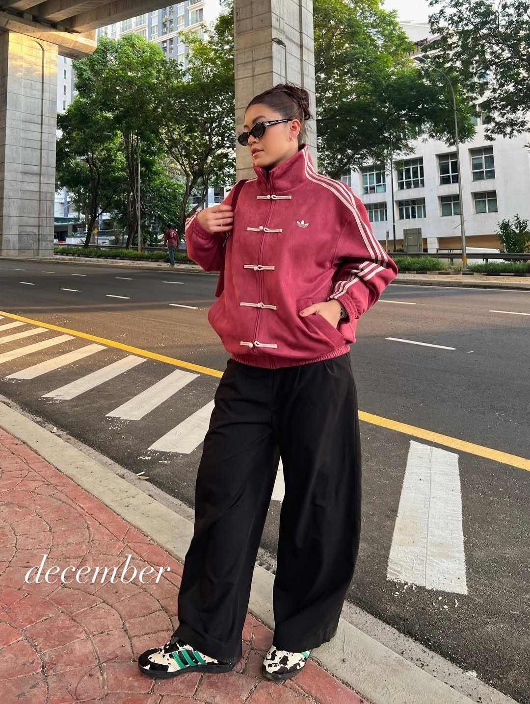 Modelo posa com jaqueta vinho em veludo com nó chinês branco, calça preta ampla e tênis estampado, em clima urbano e