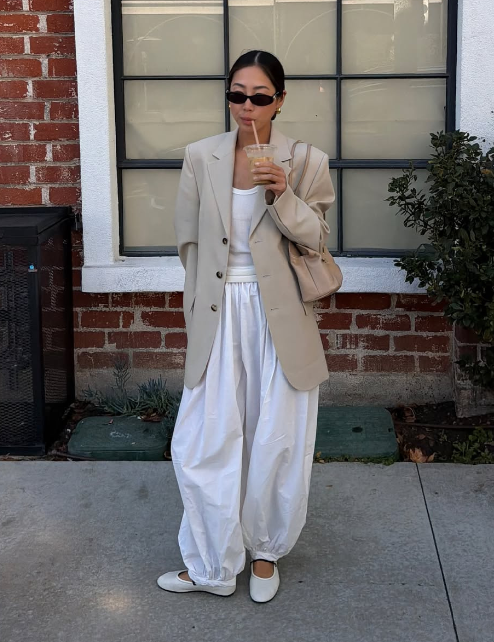 Modelo posa com novos looks minimalistas em blazer bege oversized, regata branca, calça ampla de algodão e sapatilha, em