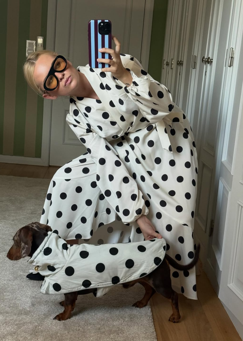 Modelo posa agachada com vestido branco de bolinhas pretas e óculos máscara oversized com lentes âmbar.