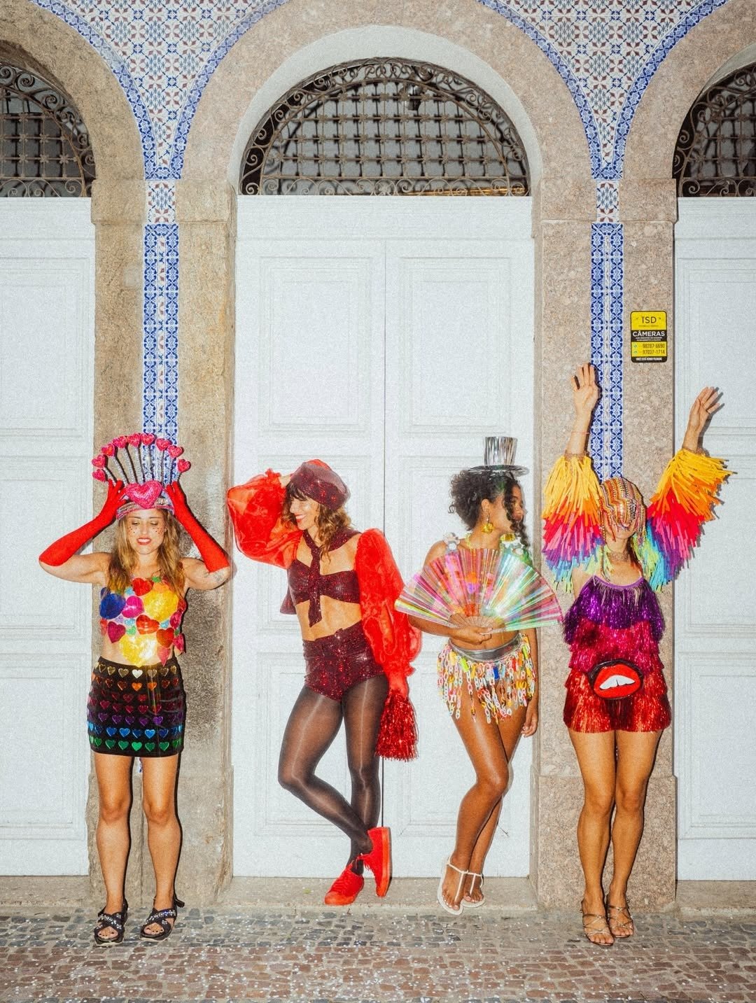 Quatro mulheres vestem fantasias vibrantes com brilhos, franjas coloridas, acessórios criativos e posam animadas, ideal para