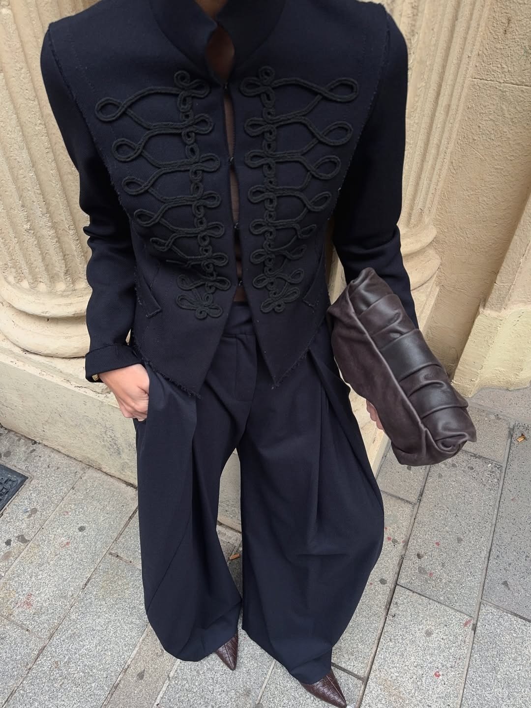 Look sofisticado em preto com blazer estruturado e nó chinês frontal, calça ampla de alfaiataria e clutch marrom, postura