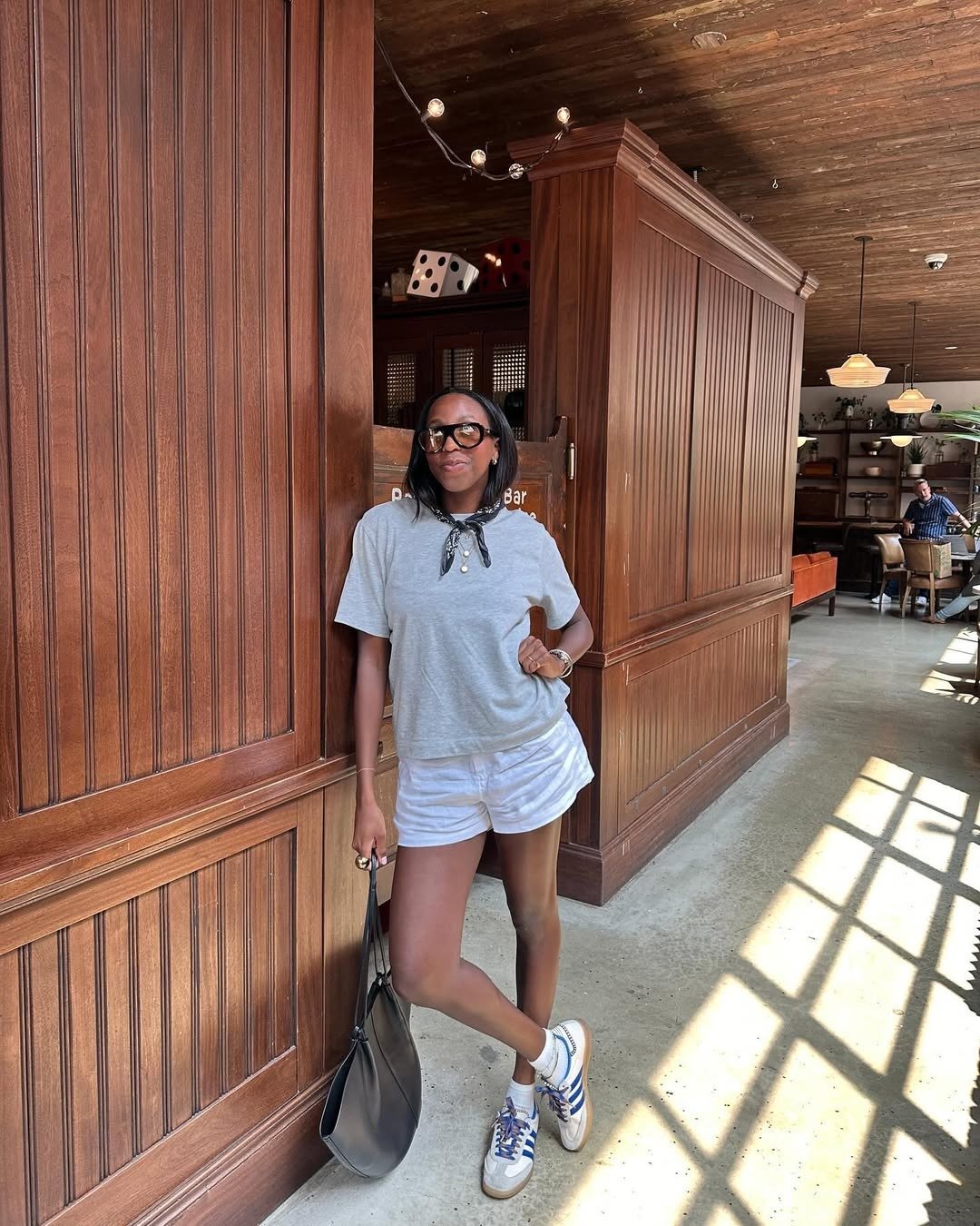 Looks com amarração no pescoço em lenço preto estampado, camiseta cinza básica, shorts branco e tênis casual