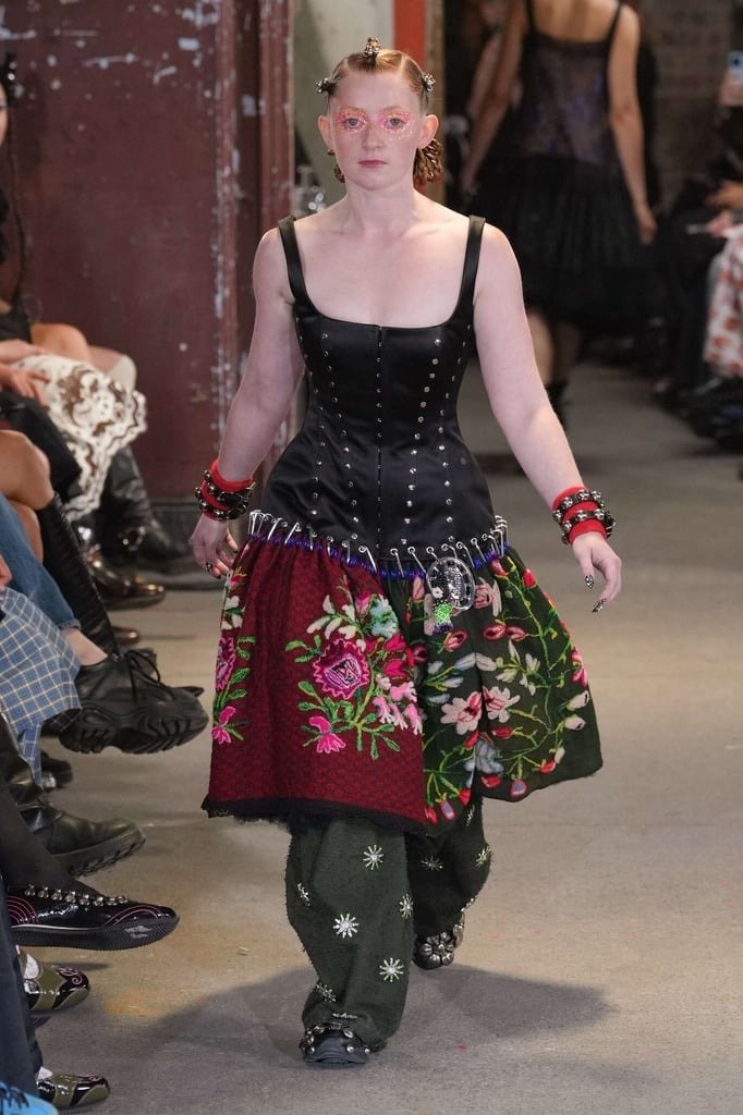 Modelo posa com saia floral em patchwork presa por pingentes para saias metálicos, combinando com corpete preto estruturado