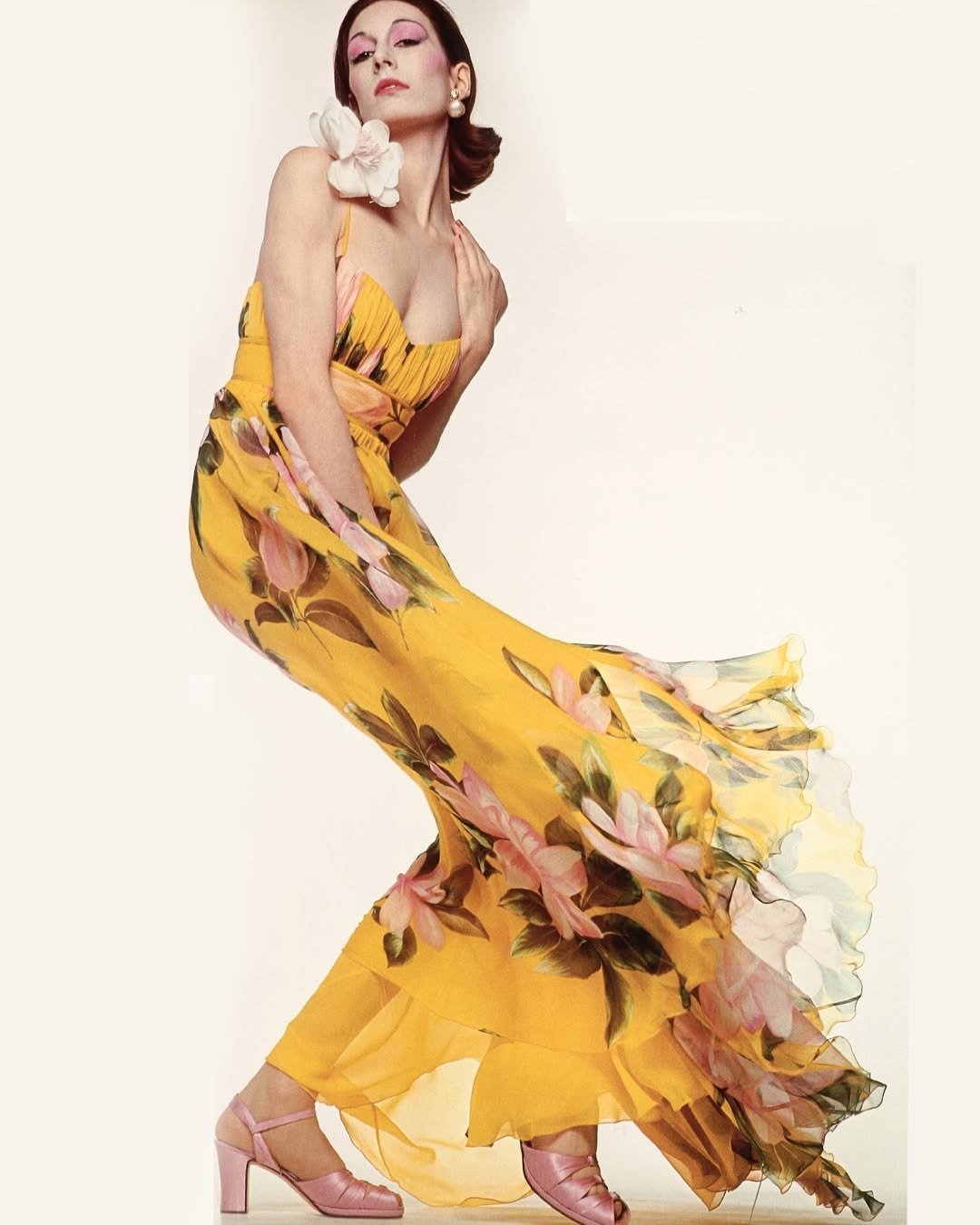 Modelo posa com vestido longo Valentino amarelo de tecido fluido, estampa floral em rosa e verde, combinando sapatos rosa e