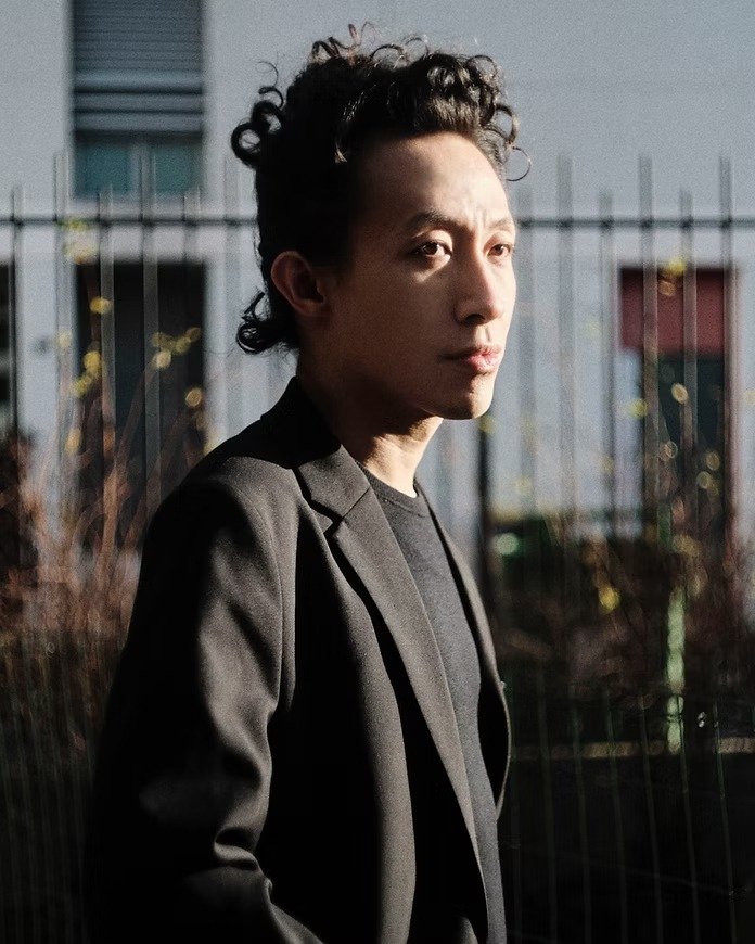 Robert Wun veste blazer preto estruturado com camiseta preta, posando de perfil em luz natural que destaca expressão