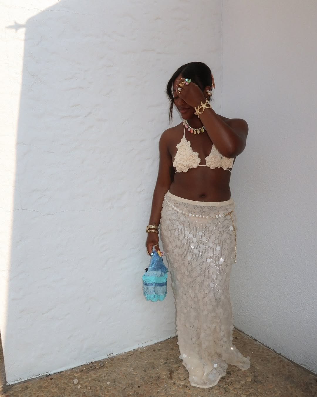 Modelo posa com saia de paetê longa bege, top de crochê e acessórios dourados, em clima leve e praiano.