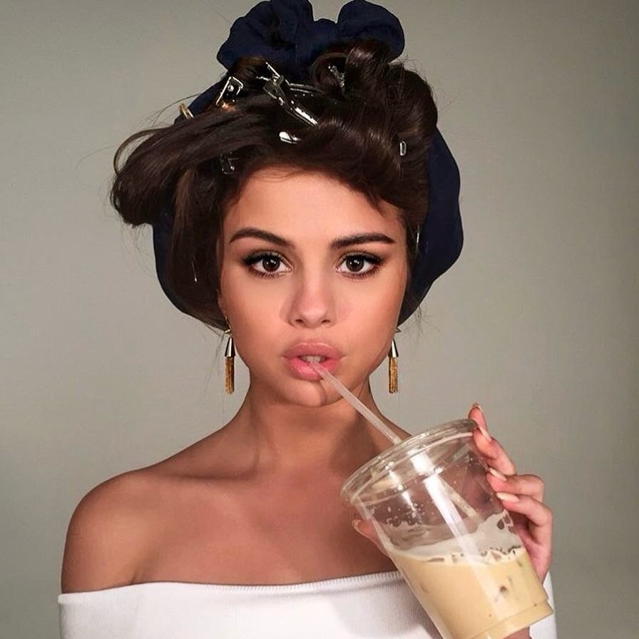 Modelo posa com expressão suave, usando top ombro a ombro branco, brincos dourados e penteado vintage com presilhas,