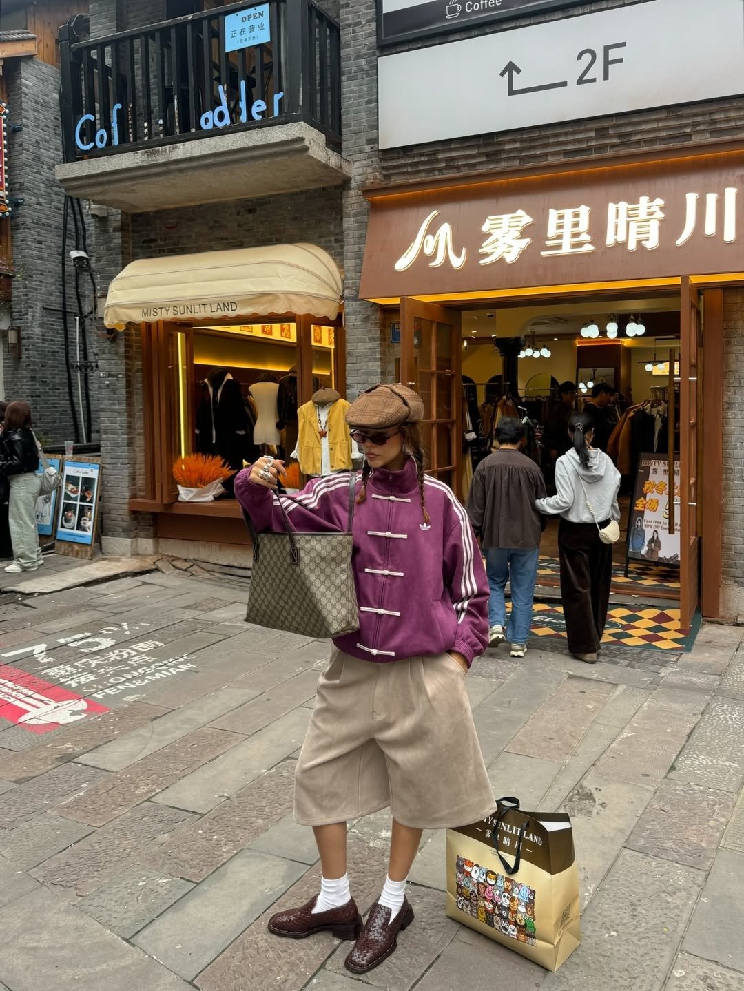 Modelo posa com jaqueta roxa de veludo com nó chinês branco, bermuda bege, sapato marrom texturizado e boina marrom em rua