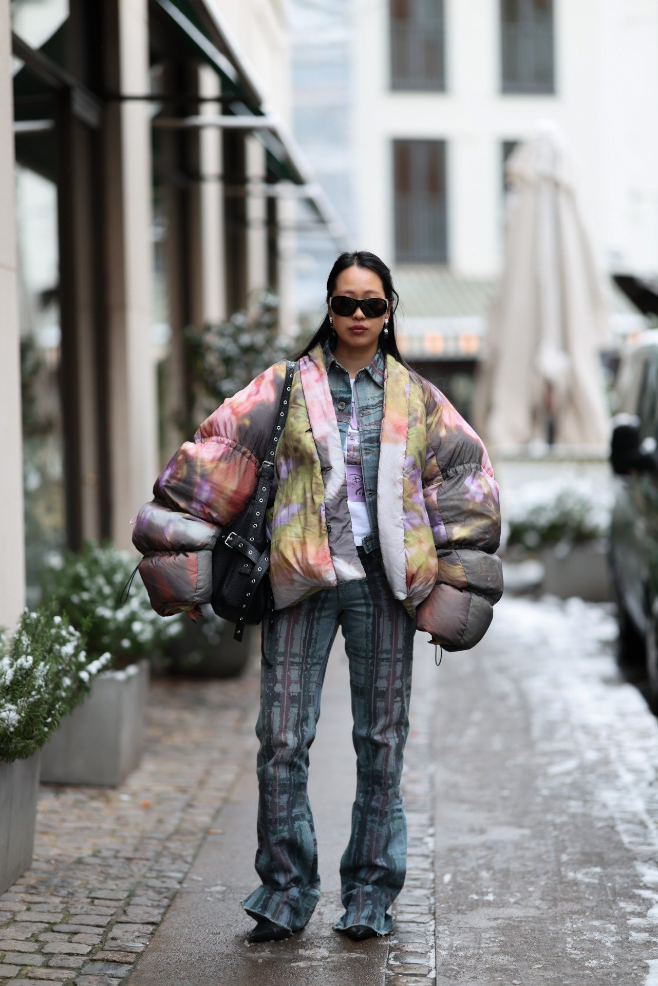 Modelo posa com jaqueta oversized em tie-dye colorido, calça flare estampada e acessórios escuros na Semana de Moda de