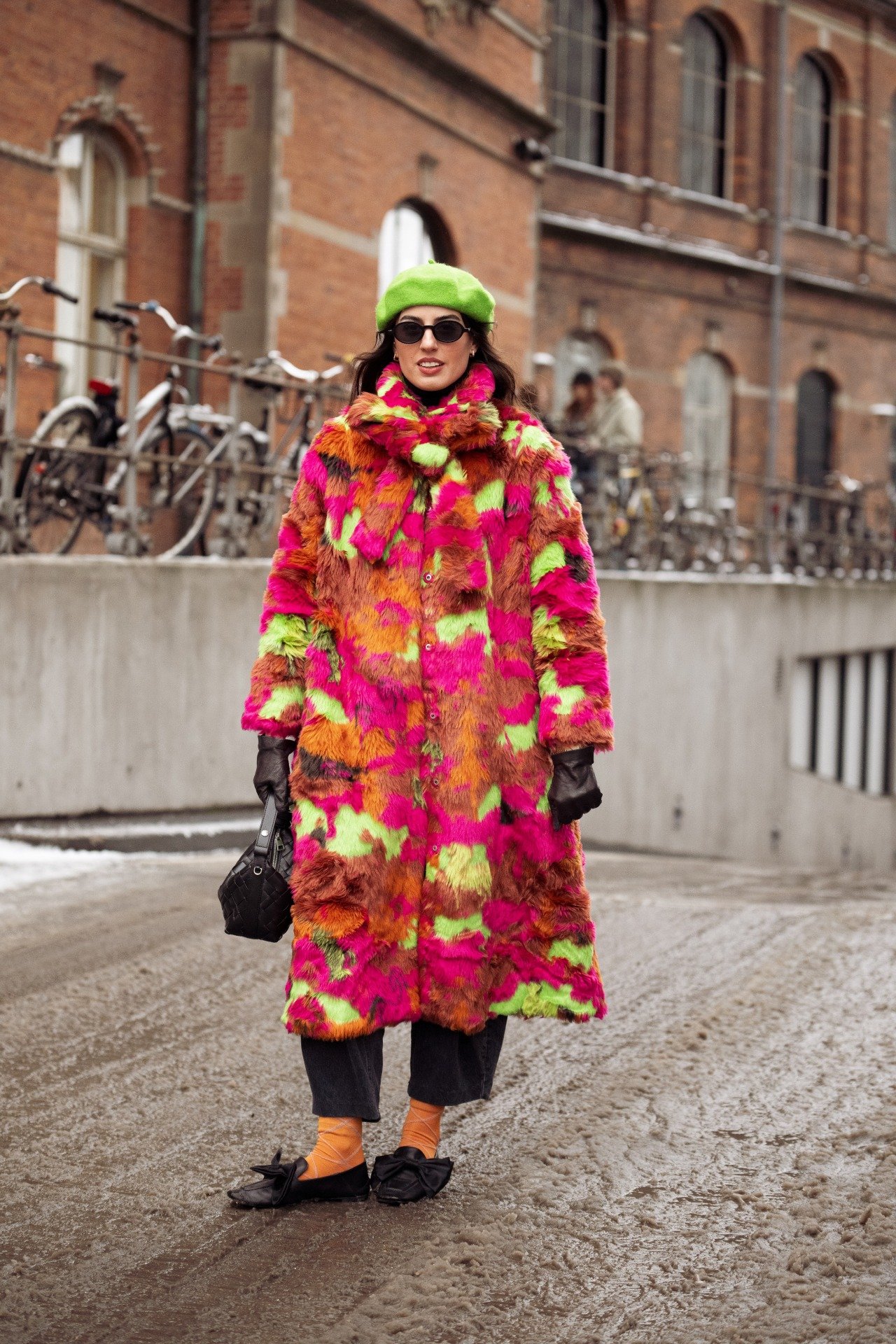 Modelo posa na Semana de Moda de Copenhagen com casaco longo peludo em tons vibrantes de rosa, laranja e verde, boina verde
