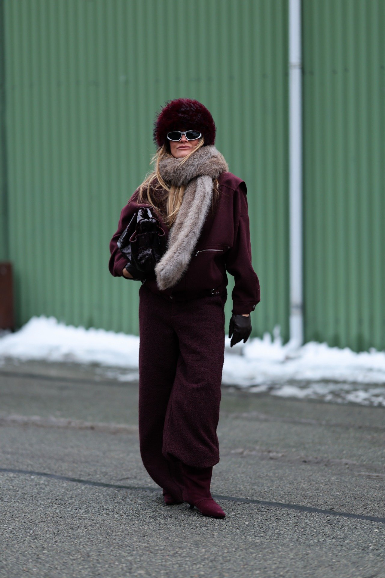 Na Semana de Moda de Copenhagen, modelo posa com look bordô oversized em tecidos texturizados, cachecol de pele e acessórios