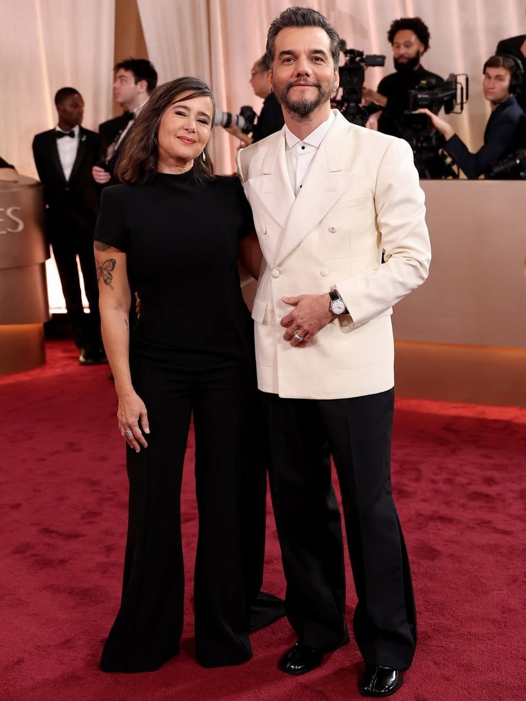 Homem posa com blazer branco e calça preta elegante, calçando sapatos Tabi pretos que destacam o estilo sofisticado e