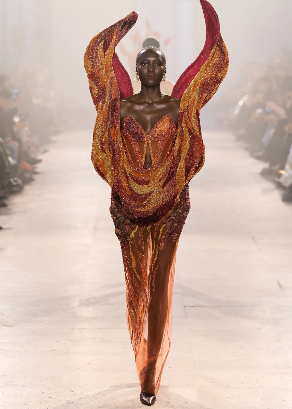 Modelo caminha com vestido fluido de alta-costura primavera 2026 em tons quentes e brilhos, destacando texturas onduladas e