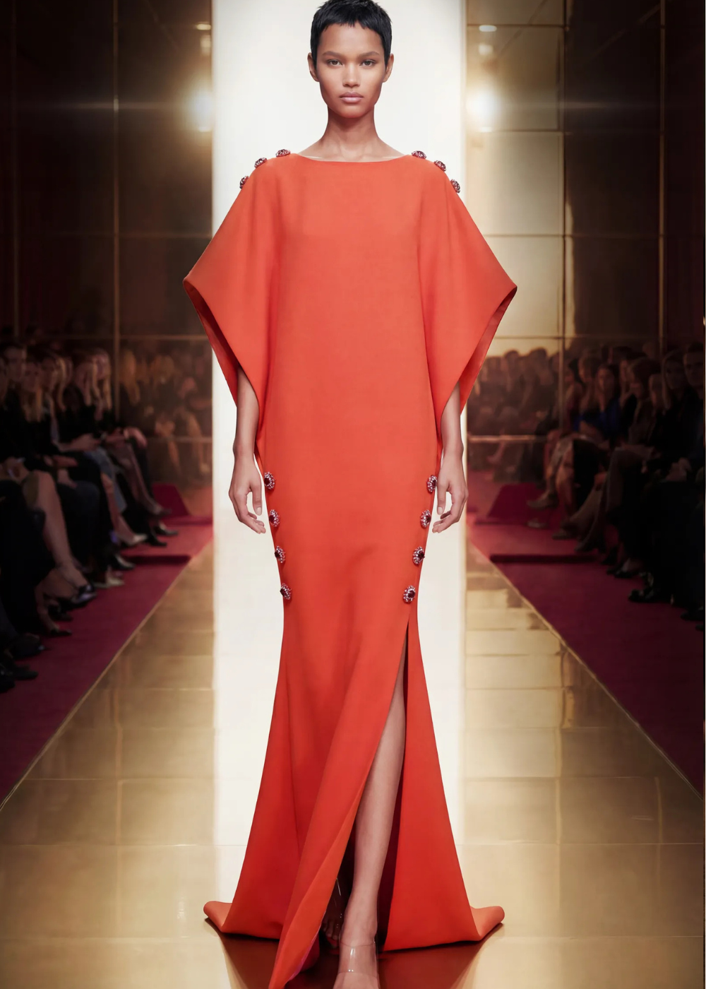 Modelo posa com vestido laranja vibrante, corte reto e fluido, detalhes em botões decorativos e fenda frontal, tendência da