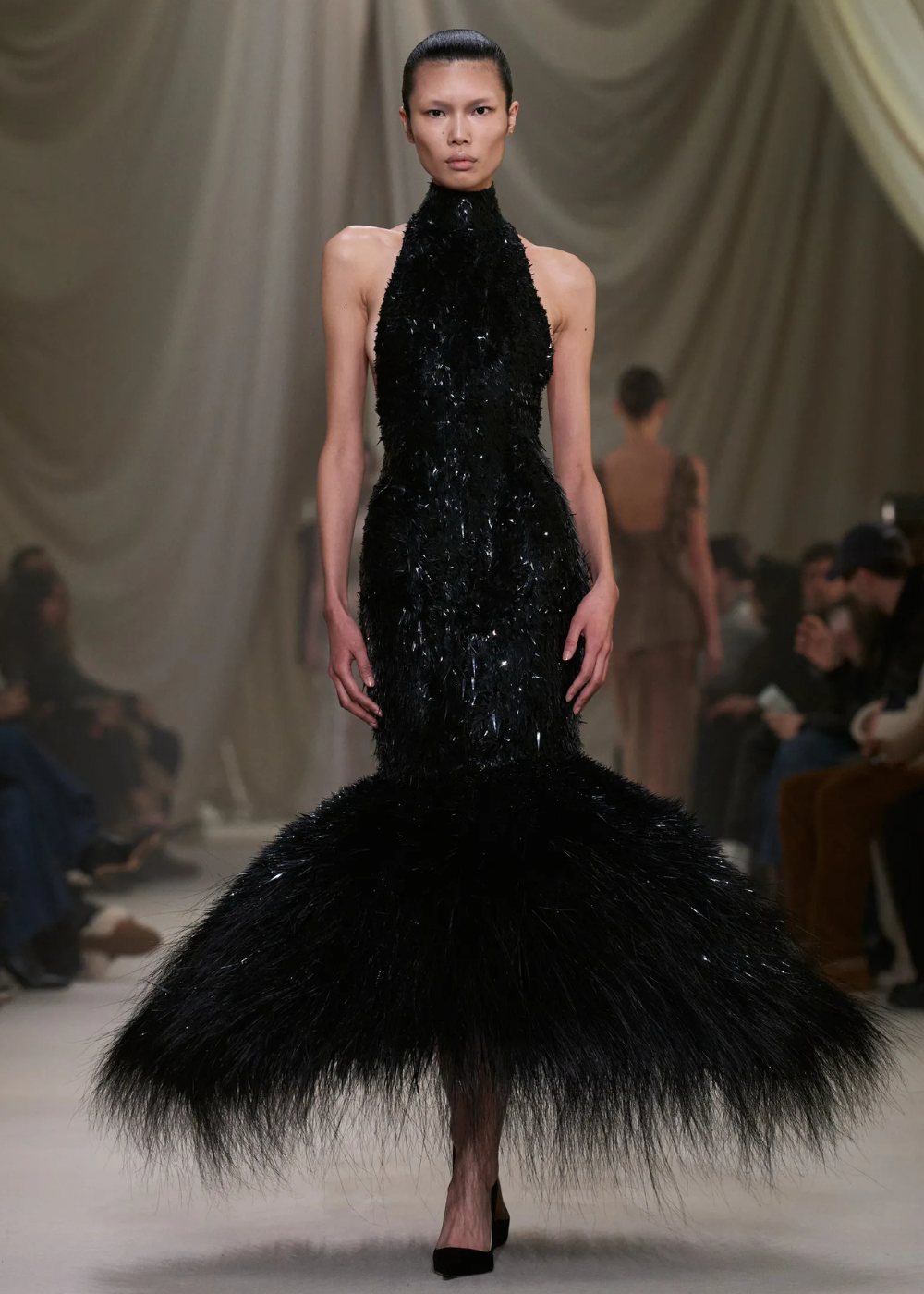 Modelo posa com vestido preto de alta-costura primavera 2026, modelagem sereia com textura brilhante e barra volumosa em