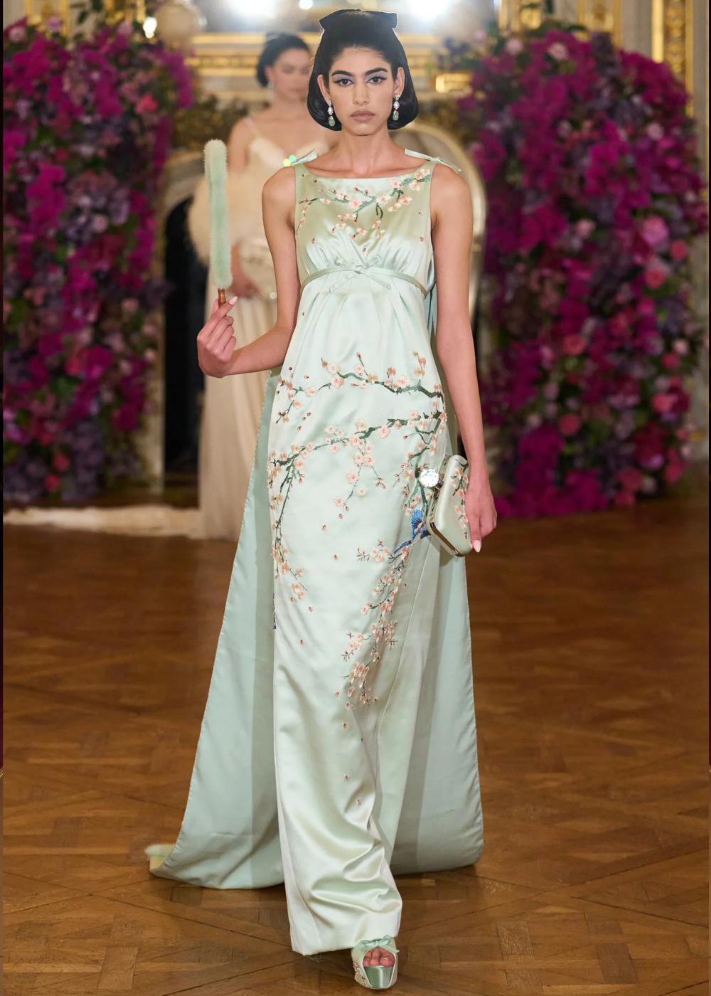 Modelo posa com vestido longo de cetim verde-água bordado com flores delicadas, acessórios elegantes e clima sereno nas