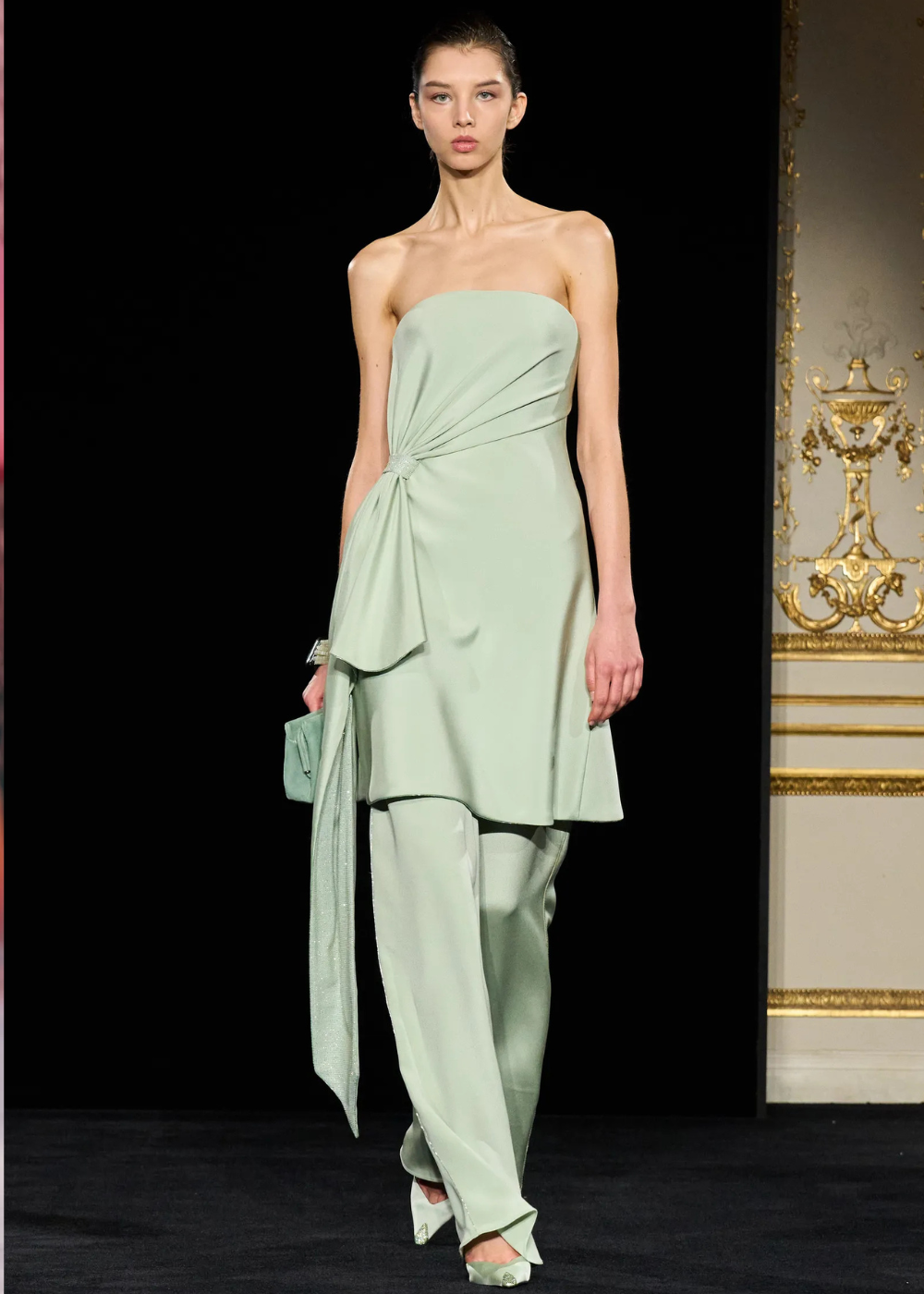 Modelo posa com vestido tomara que caia e calça fluida em verde menta, destacando drapeados e tecidos leves nas tendências