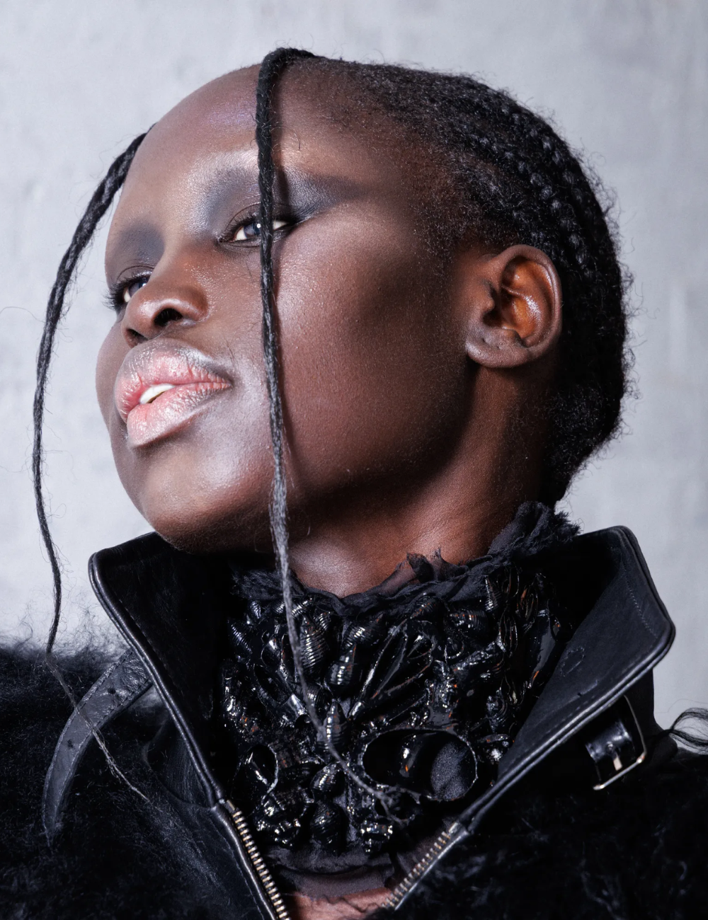 Modelo posa com maquiagem futurista em tons metálicos e look preto com texturas ricas, destacando tendências de beleza 2026.