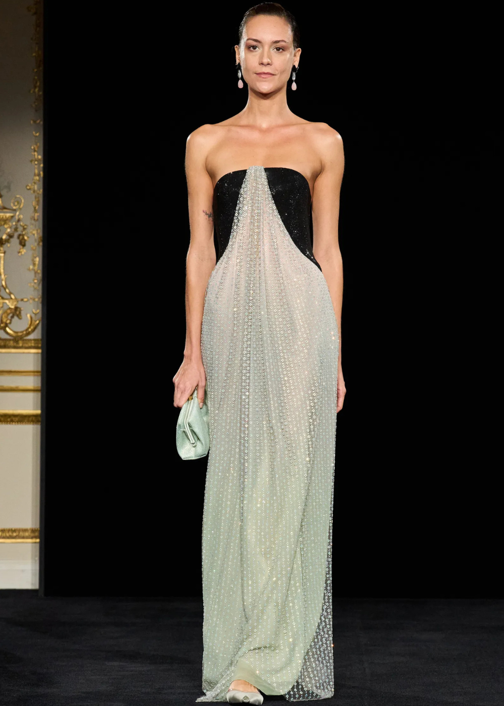 Modelo posa com vestido longo tomara que caia em preto e tule transparente cravejado de cristais, combinando clutch