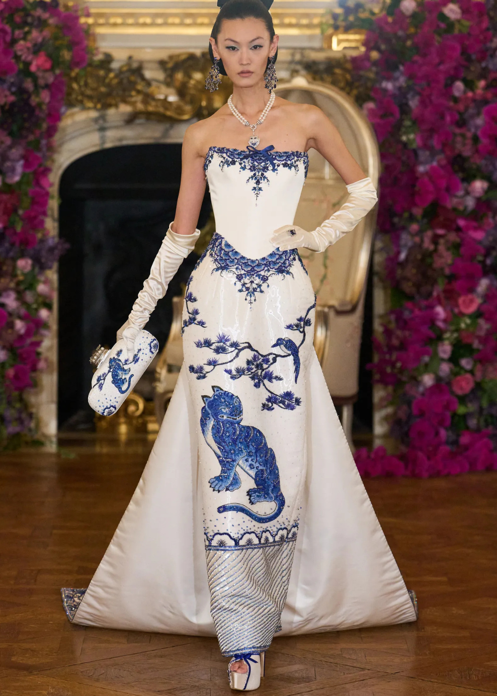 Modelo posa com vestido tomara que caia branco em cetim, bordados azuis de tigre e pássaro, luvas longas e clutch,