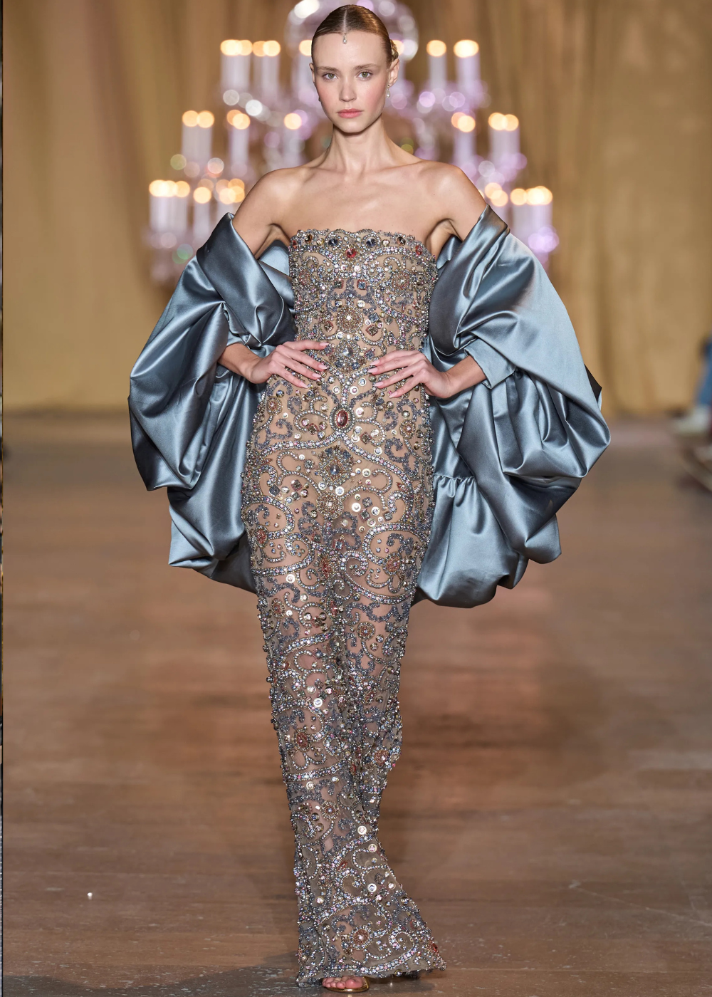 Modelo posa com vestido justo transparente bordado em cristais e pedrarias, acompanhado de capa azul metálica, refletindo