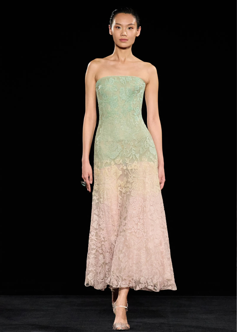 Modelo posa com vestido tomara que caia de renda degradê verde e rosa pastel, evidenciando delicadeza e sofisticação nas