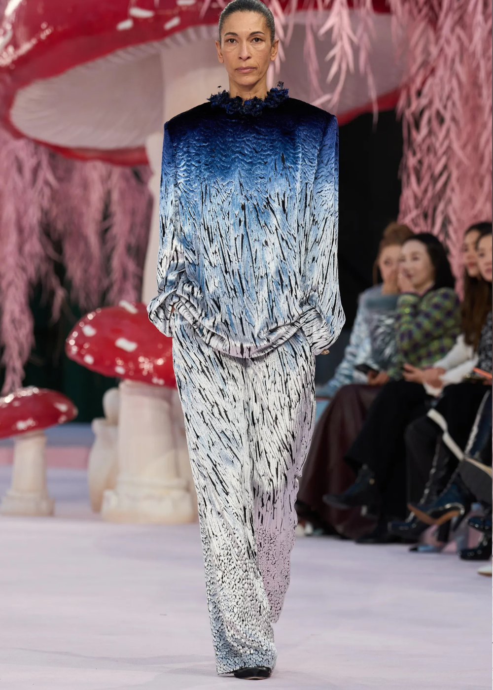 Modelo caminha com postura firme usando conjunto de veludo degradê azul e branco com textura marcante, refletindo tendências