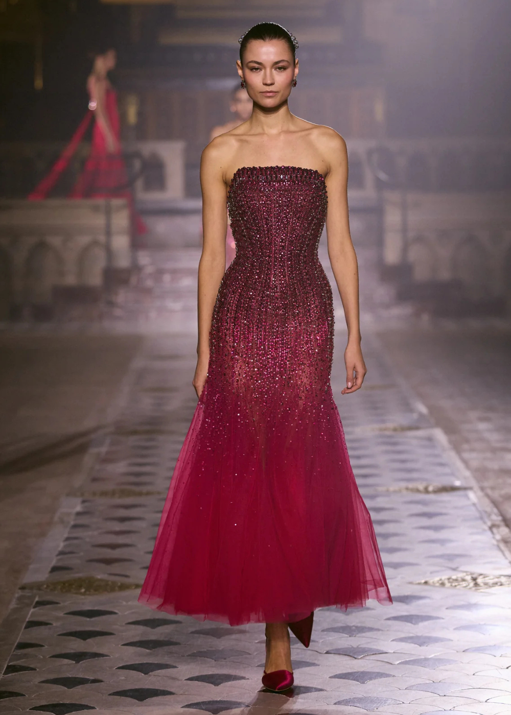 Modelo caminha com postura confiante em vestido tomara que caia bordado em tons de vinho e rosa, combinando tule fluido e