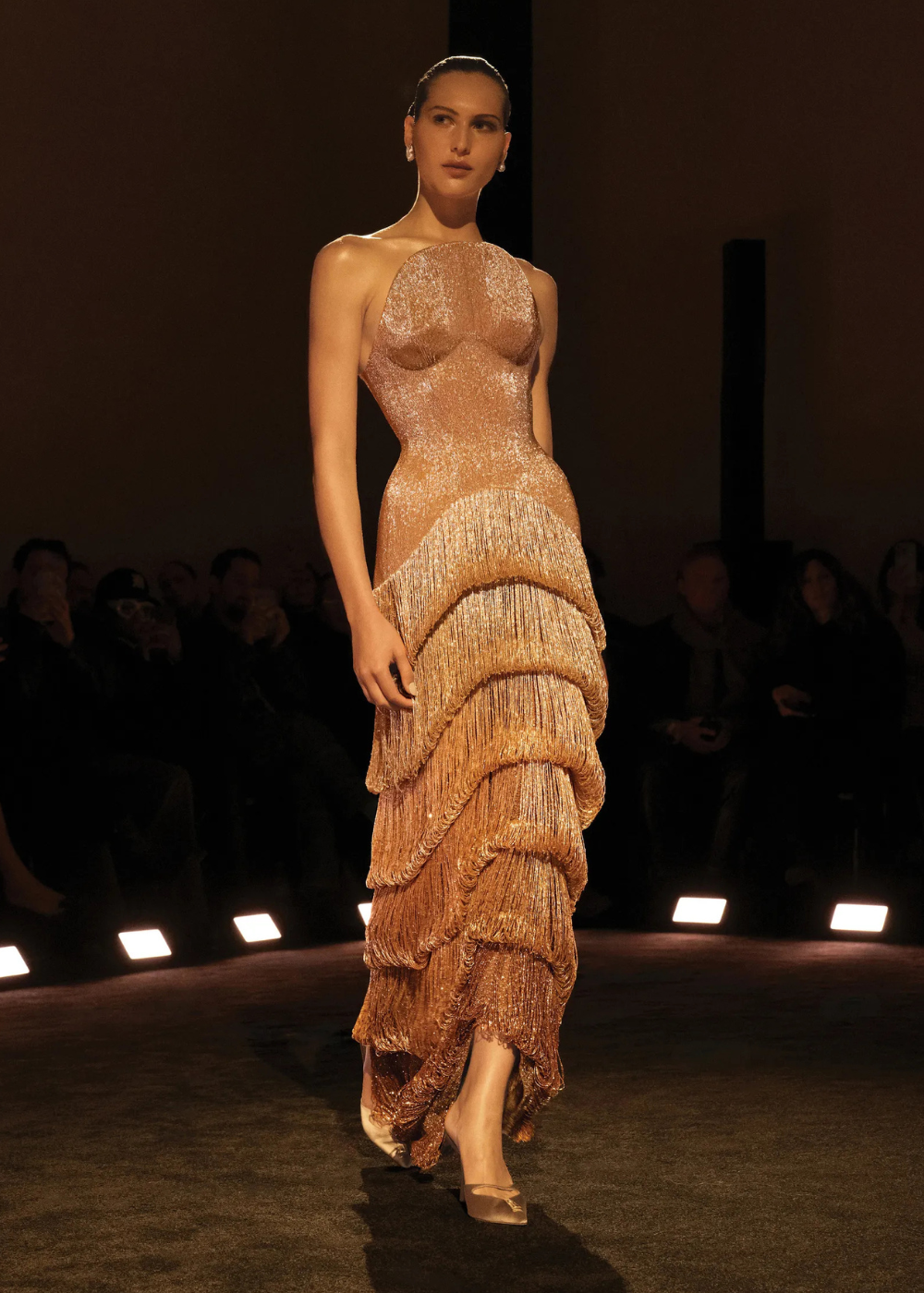 Modelo posa com vestido longo de alta-costura primavera 2026 em tecido brilhante nude, franjas em camadas e silhueta