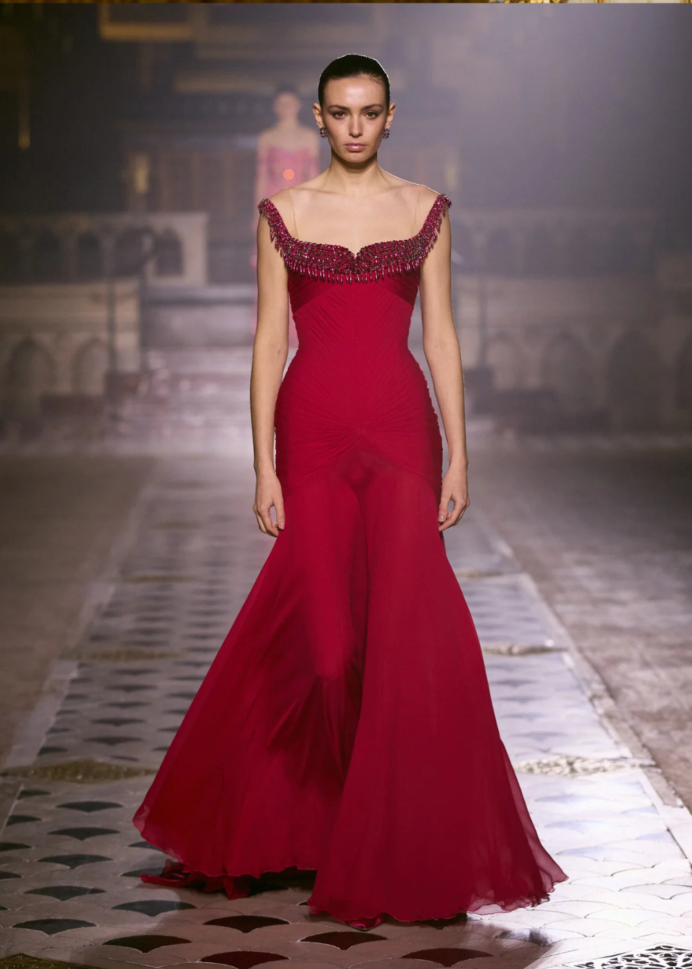 Modelo posa com vestido longo de alta-costura primavera 2026 em tom vermelho vibrante, com decote bordado e saia fluida em