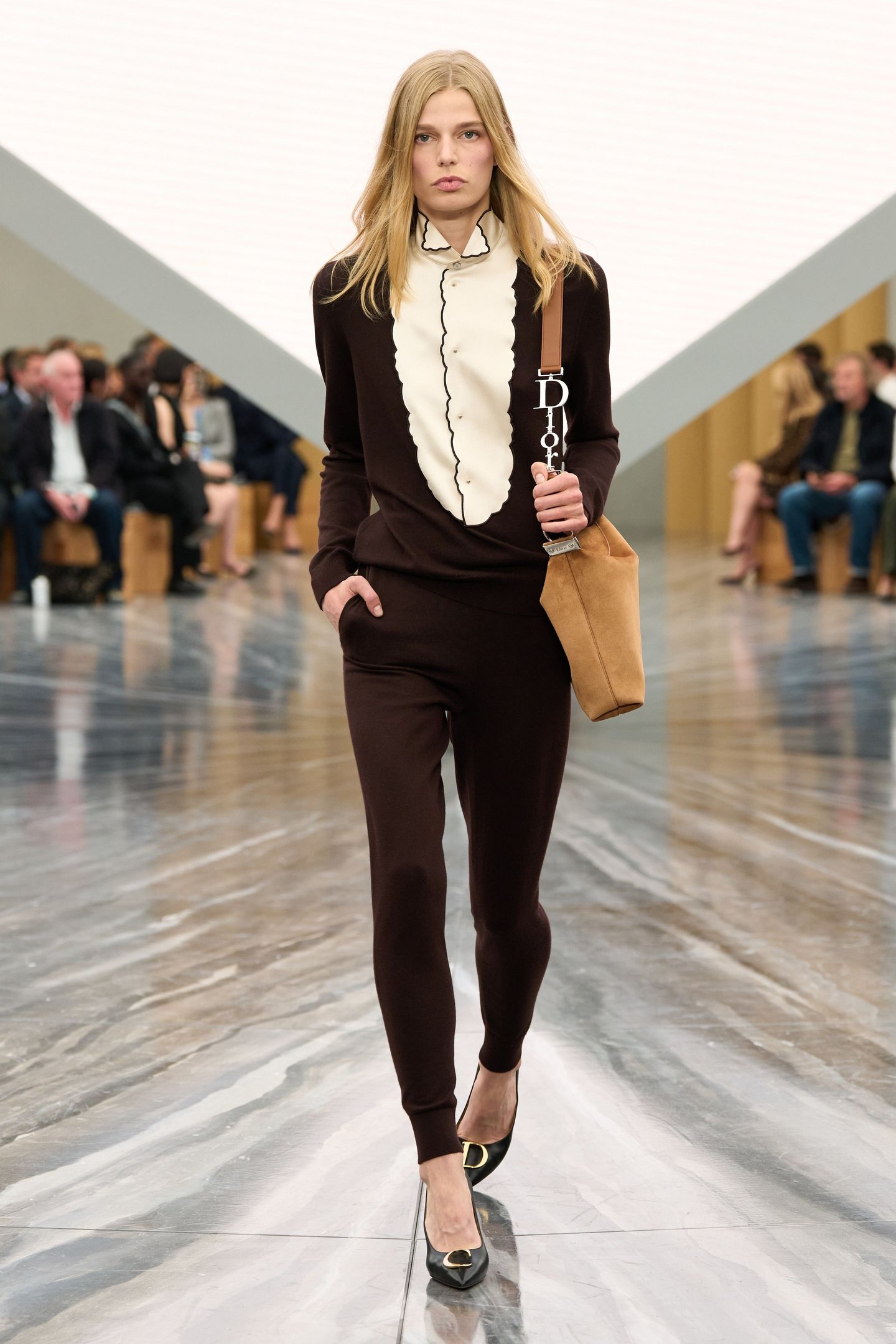 Modelo caminha com postura confiante usando calça legging marrom de tecido ajustado, combinada com blusa preta e detalhe