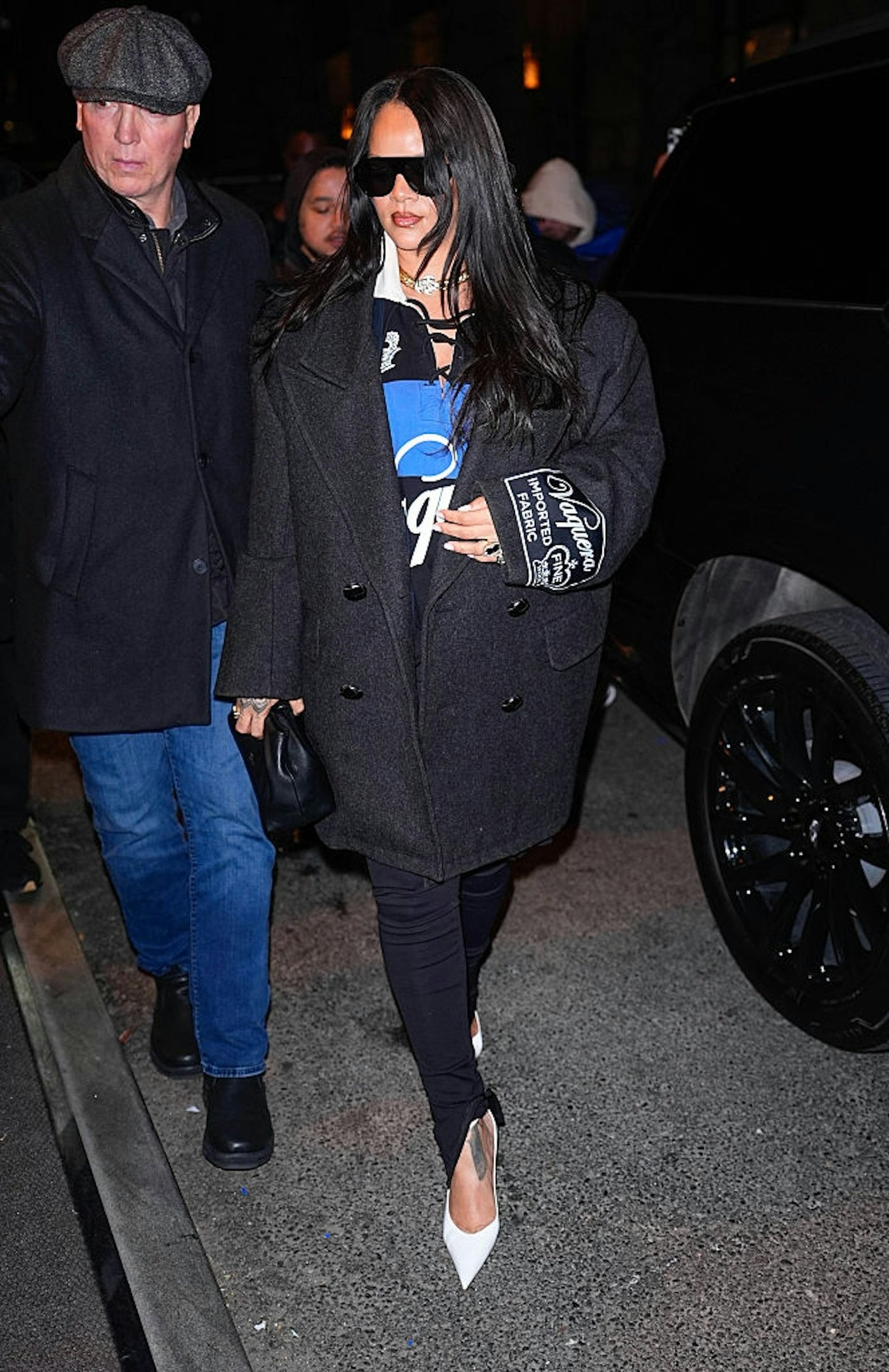 Modelo caminha com calça legging preta justa, casaco oversized cinza escuro, blusa azul e branca, e scarpin branco pontudo,