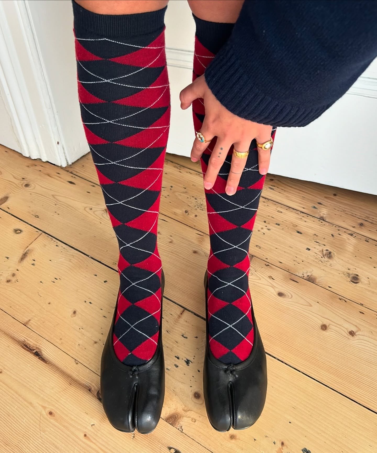 Meia alta xadrez vermelho e preto com linhas brancas, combinada a sapatos pretos de couro com bico dividido, inverno 2026