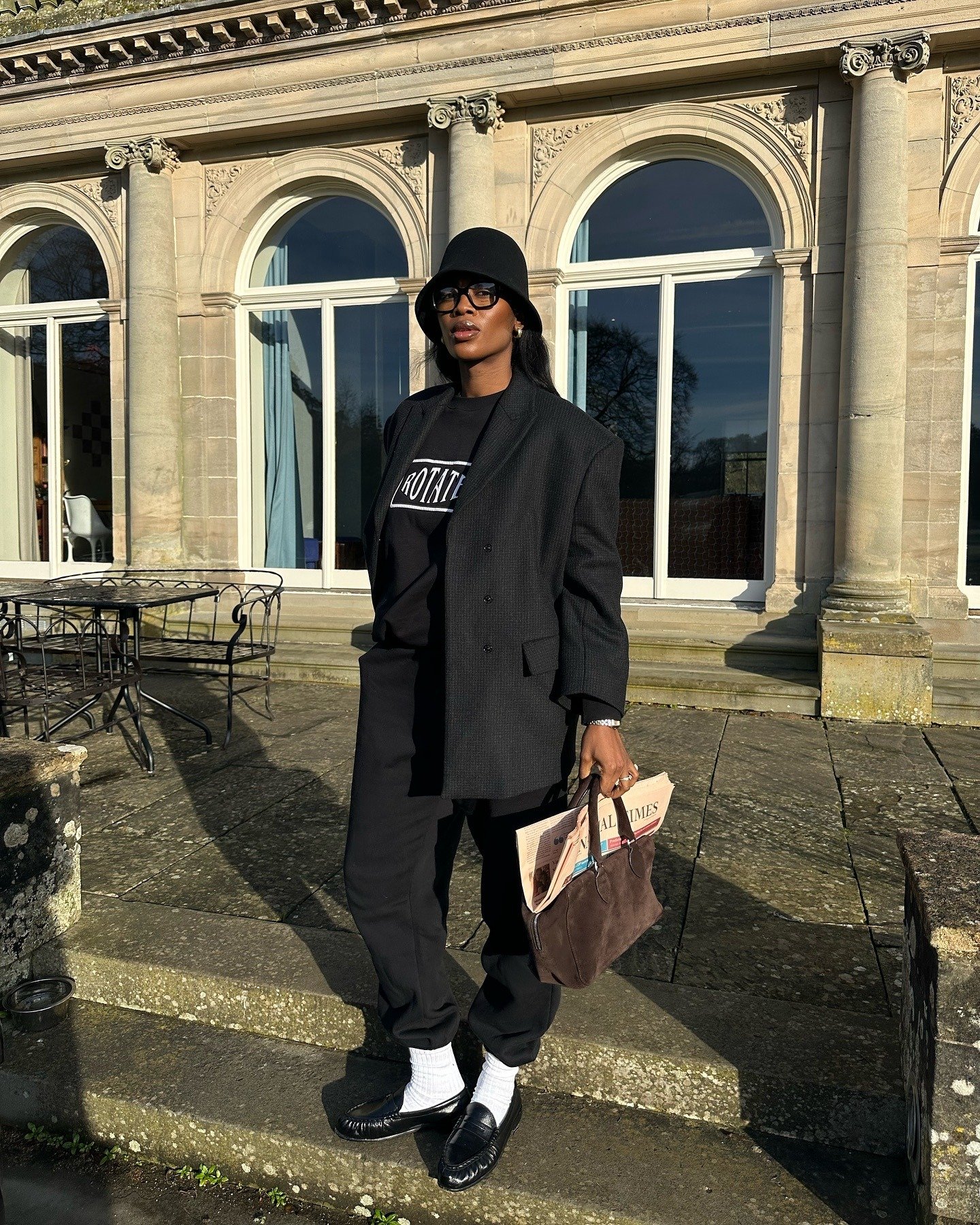 Modelo posa com blazer oversized, calça jogger e camiseta preta, chapéu bucket e loafers, em look sofisticado para inverno