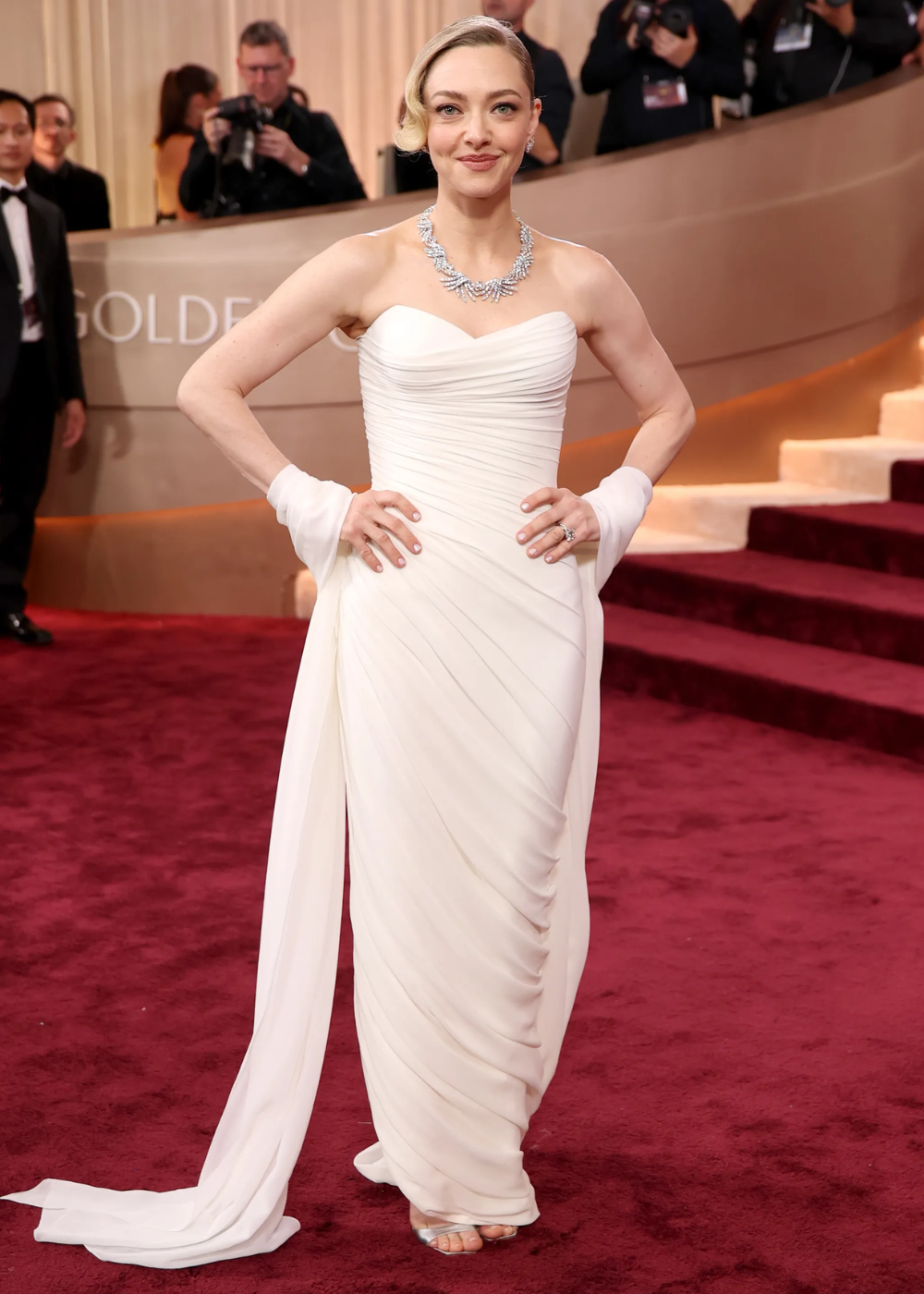 Modelo posa confiante no tapete vermelho do Globo de Ouro 2026 com vestido branco drapeado tomara que caia.